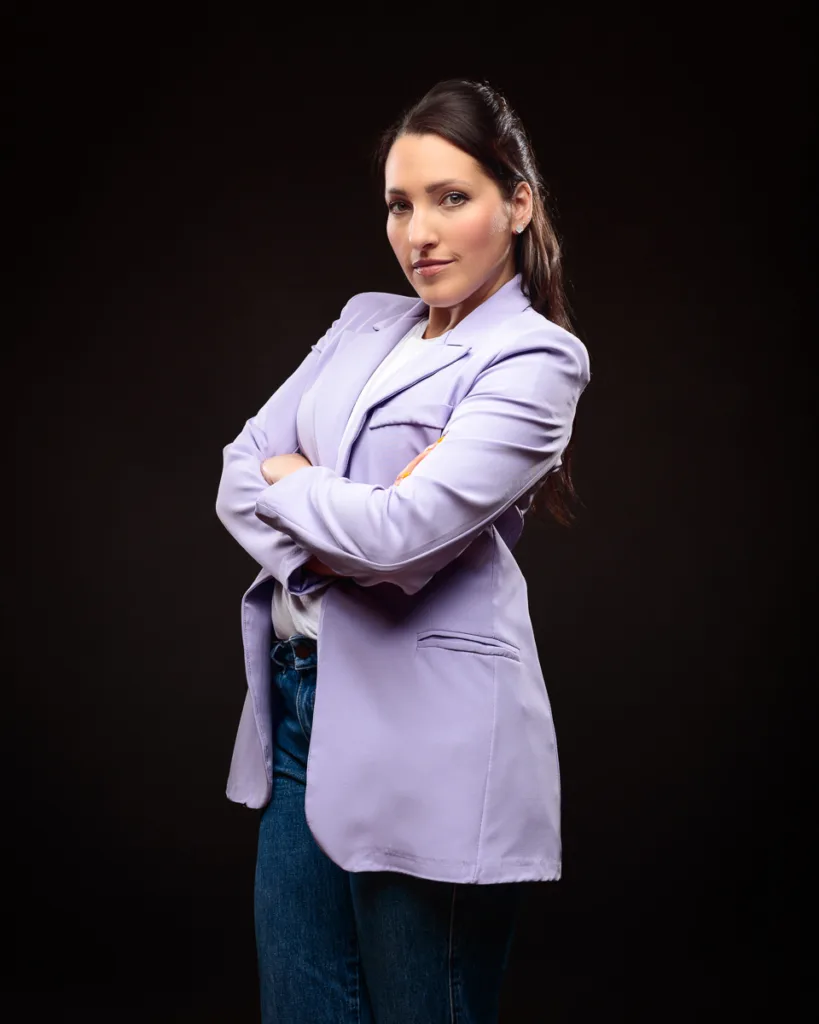 Confident woman in lavender blazer, dark background.