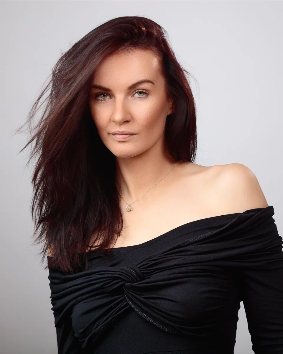 Woman in black off-shoulder dress posing confidently.