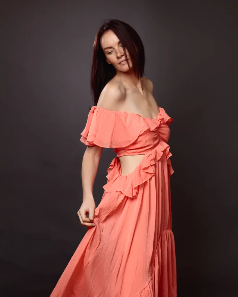 Model portfolio photograph of a woman in a coral off-shoulder ruffled dress
