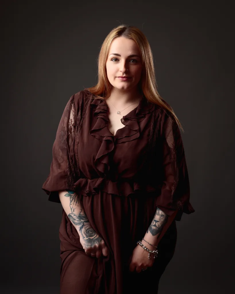 Person in brown dress with tattoos smiling.