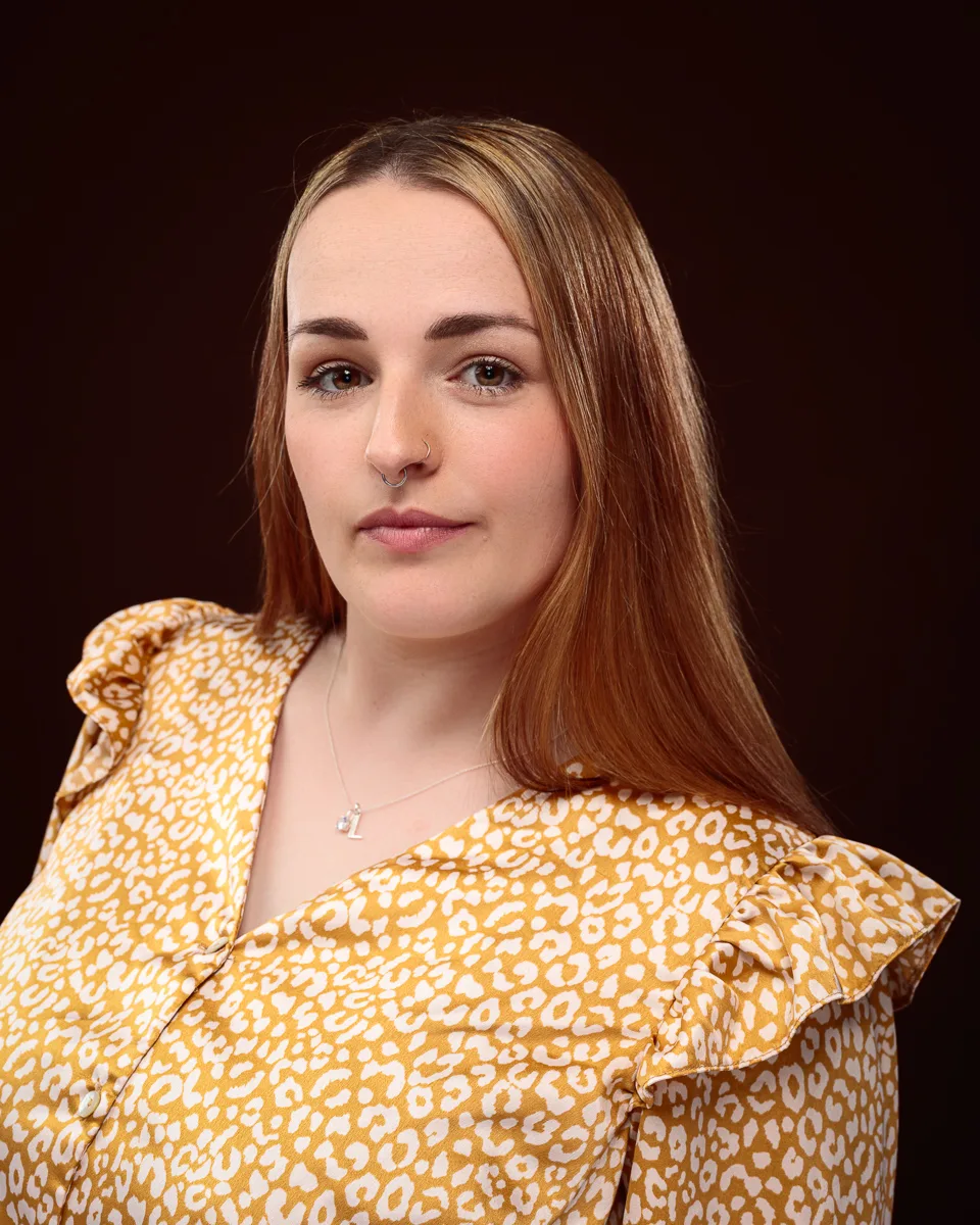 Person in yellow patterned blouse on dark background.