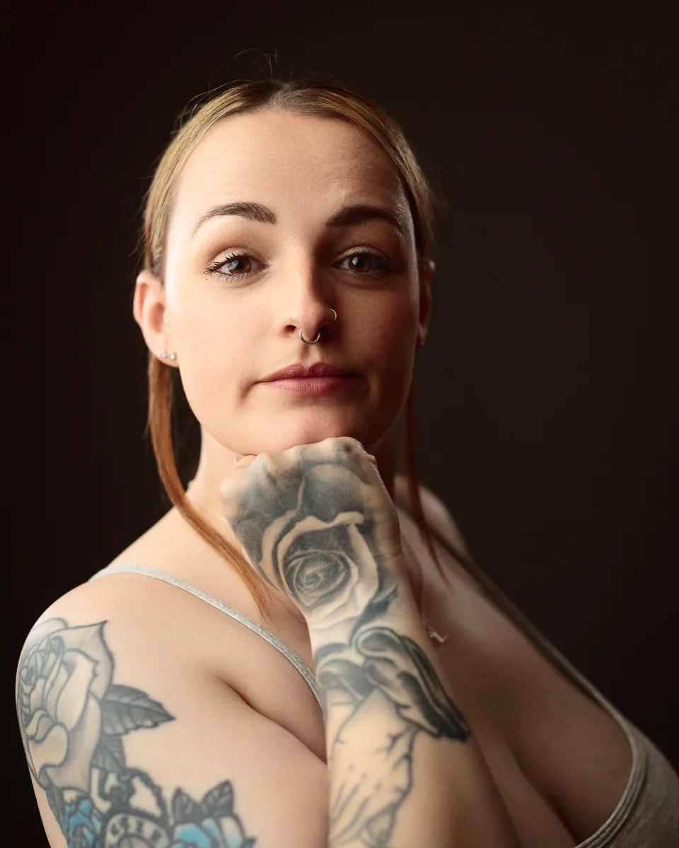 Woman with tattoos posing thoughtfully indoors.