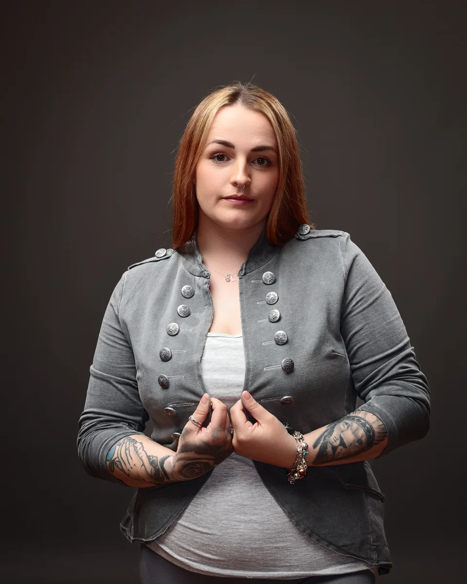 Person with tattoos wearing grey jacket, neutral background.