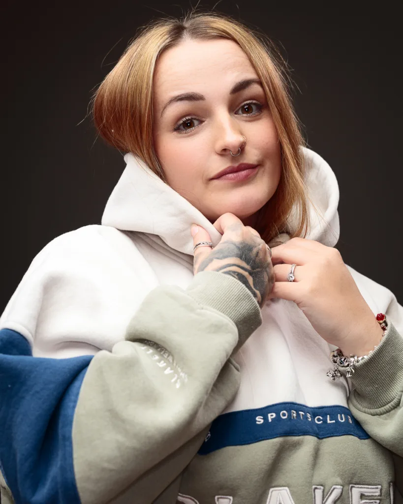 Person with hoodie, smiling, tattooed hand visible.