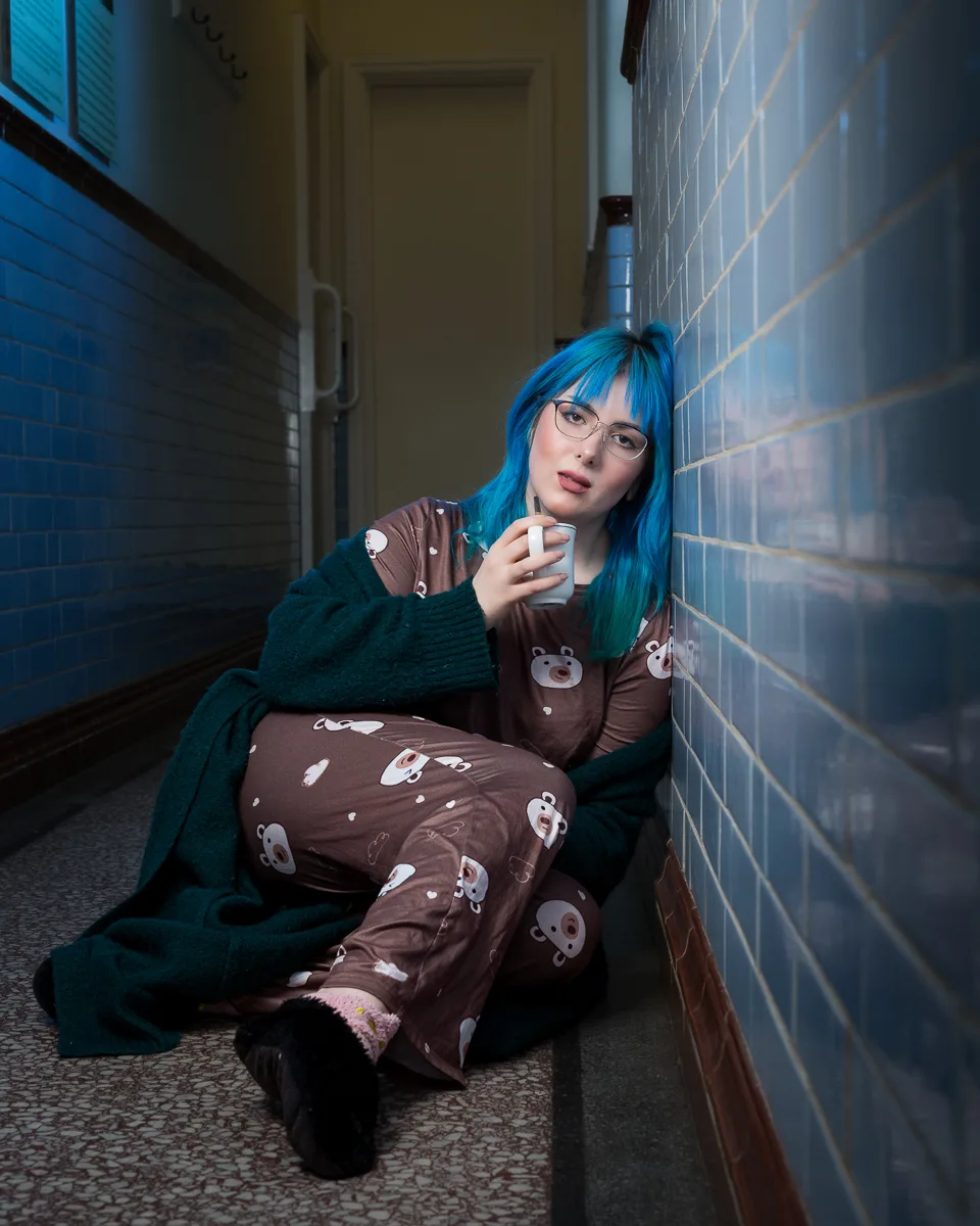 Woman with blue hair drinking coffee in hallway.