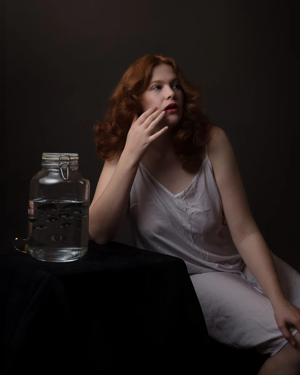 Woman in white dress beside jar with eyes design.