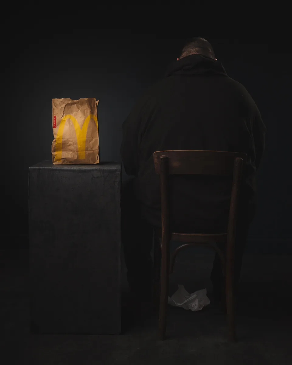 Person sitting, fast food bag on dark table.
