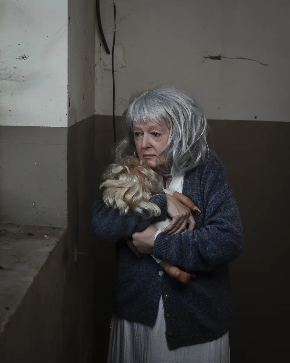 Elderly woman holding a doll in dim room.