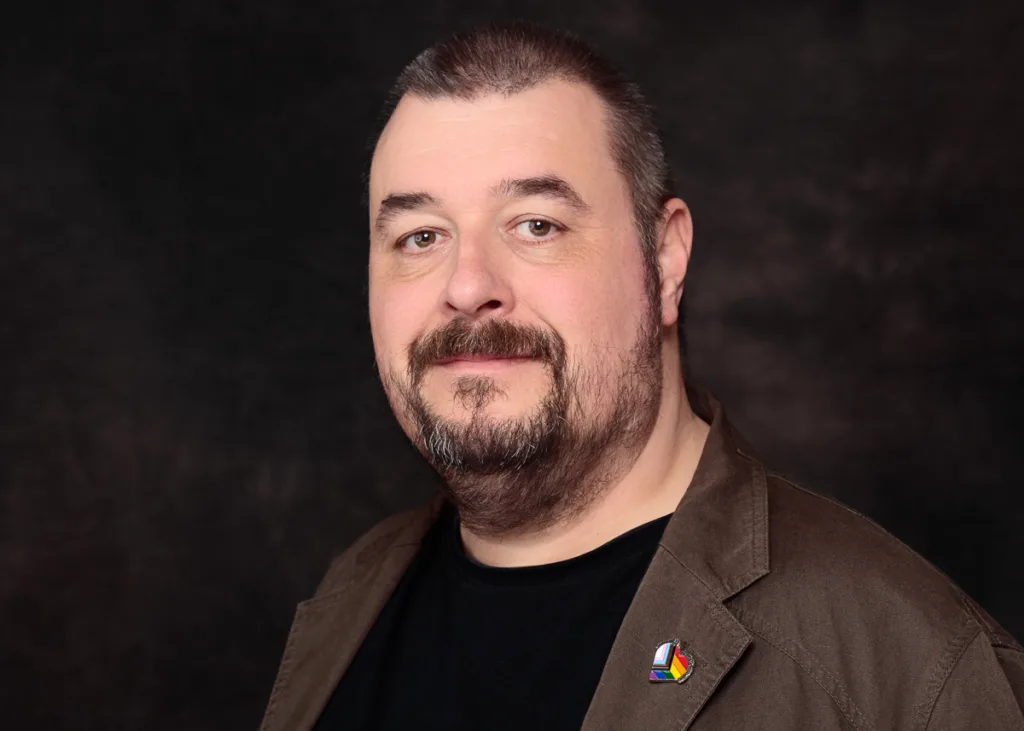 Man with beard and short hair posing, dark background.