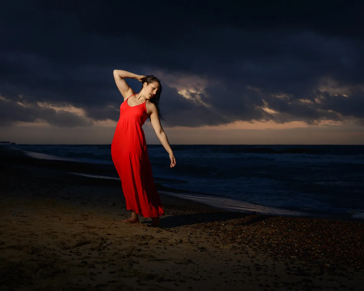 Woman in red dress poses on beach at dusk.