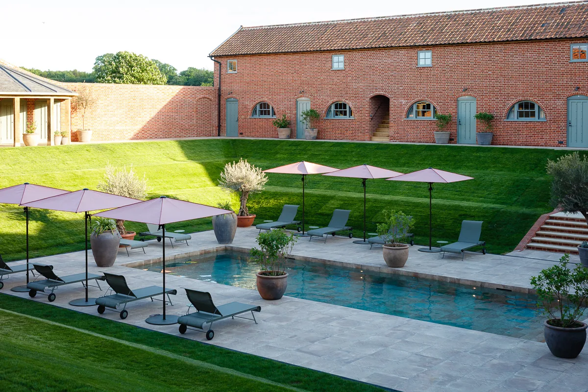 Swimming pool with sun loungers and parasols beside a converted barn