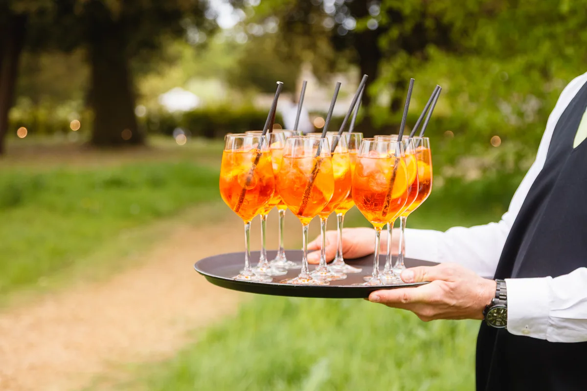 Waiter serving Aperol Spritz cocktails on a tray.
