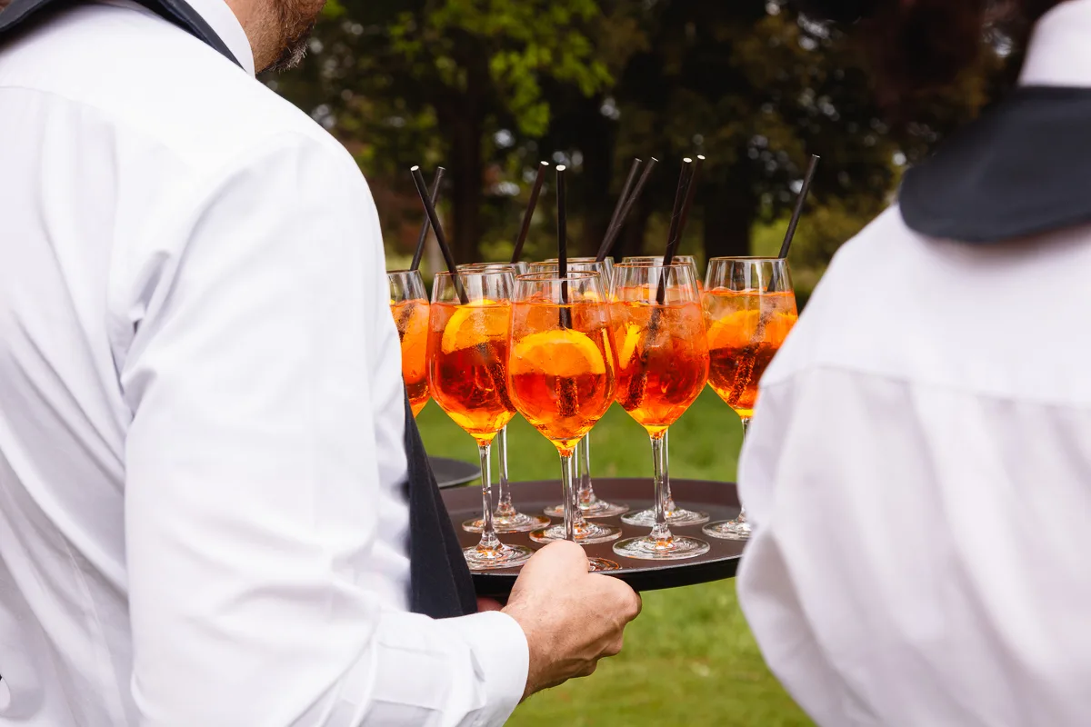 Waiters serving Aperol Spritz cocktails on a tray.