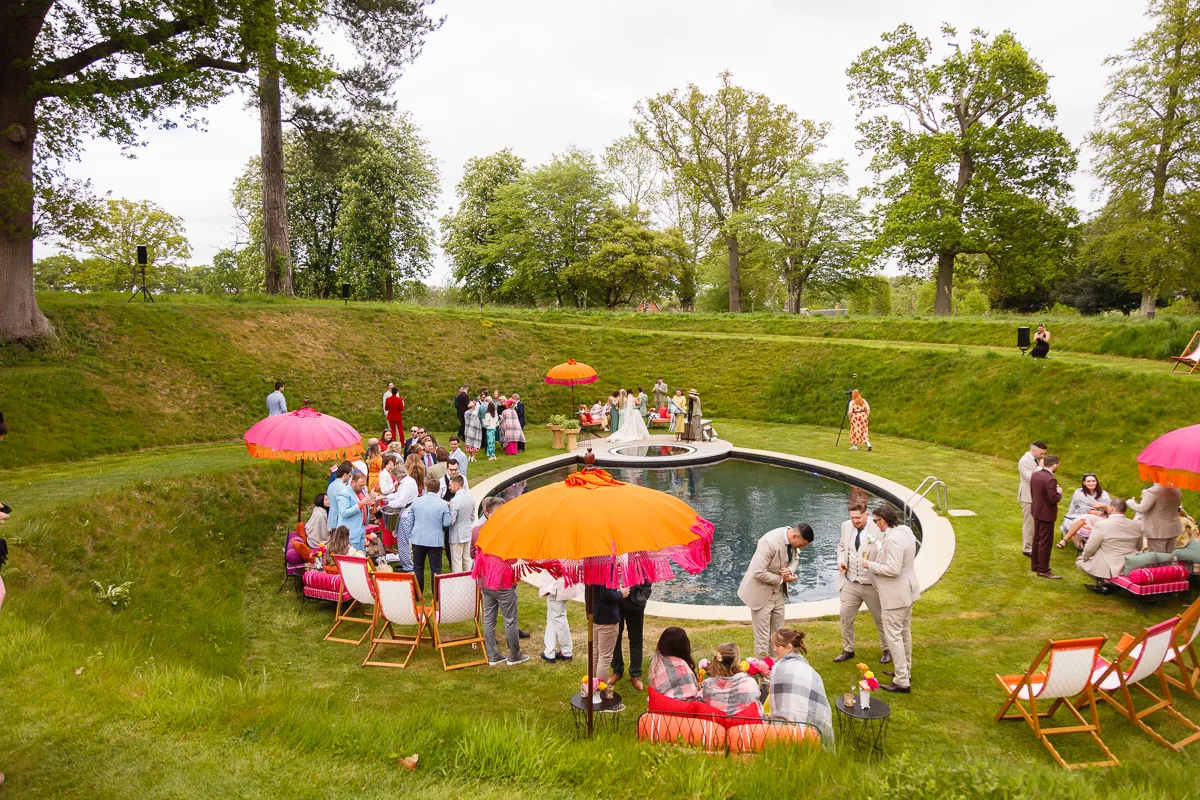 Outdoor gathering around pool with colourful umbrellas.