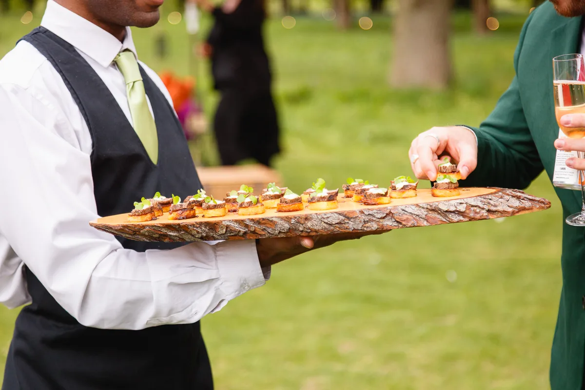 Waiter serving canapés on wooden platter at event.