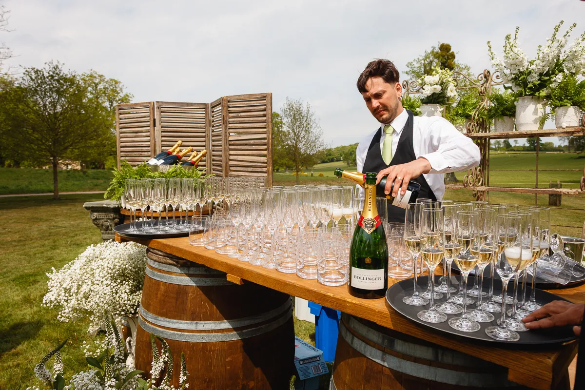 Waiter pouring champagne at outdoor event table.