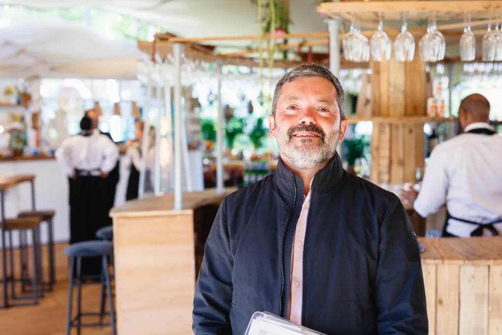 Smiling man stands in a lively restaurant bar.