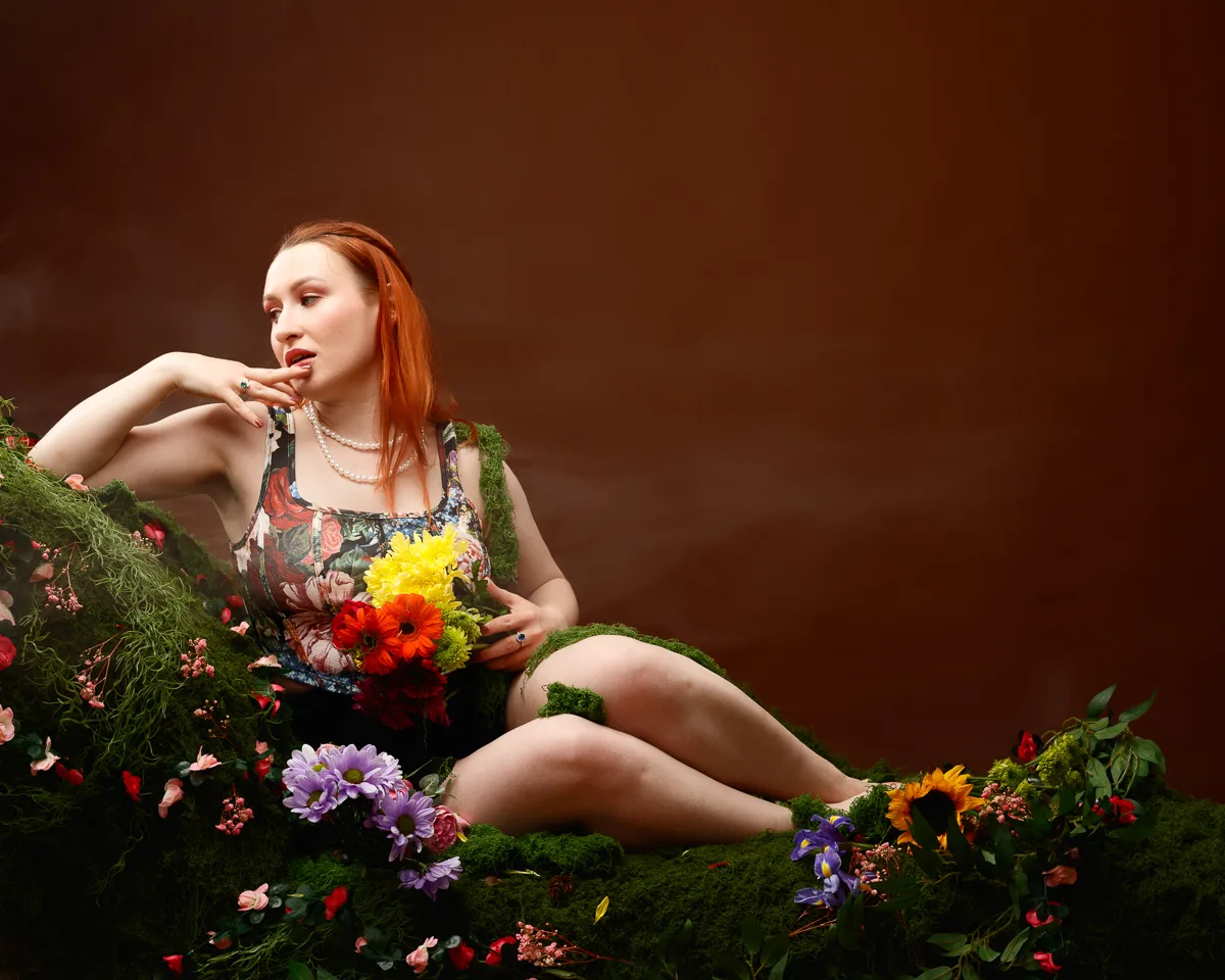 Woman surrounded by flowers on a mossy seat.