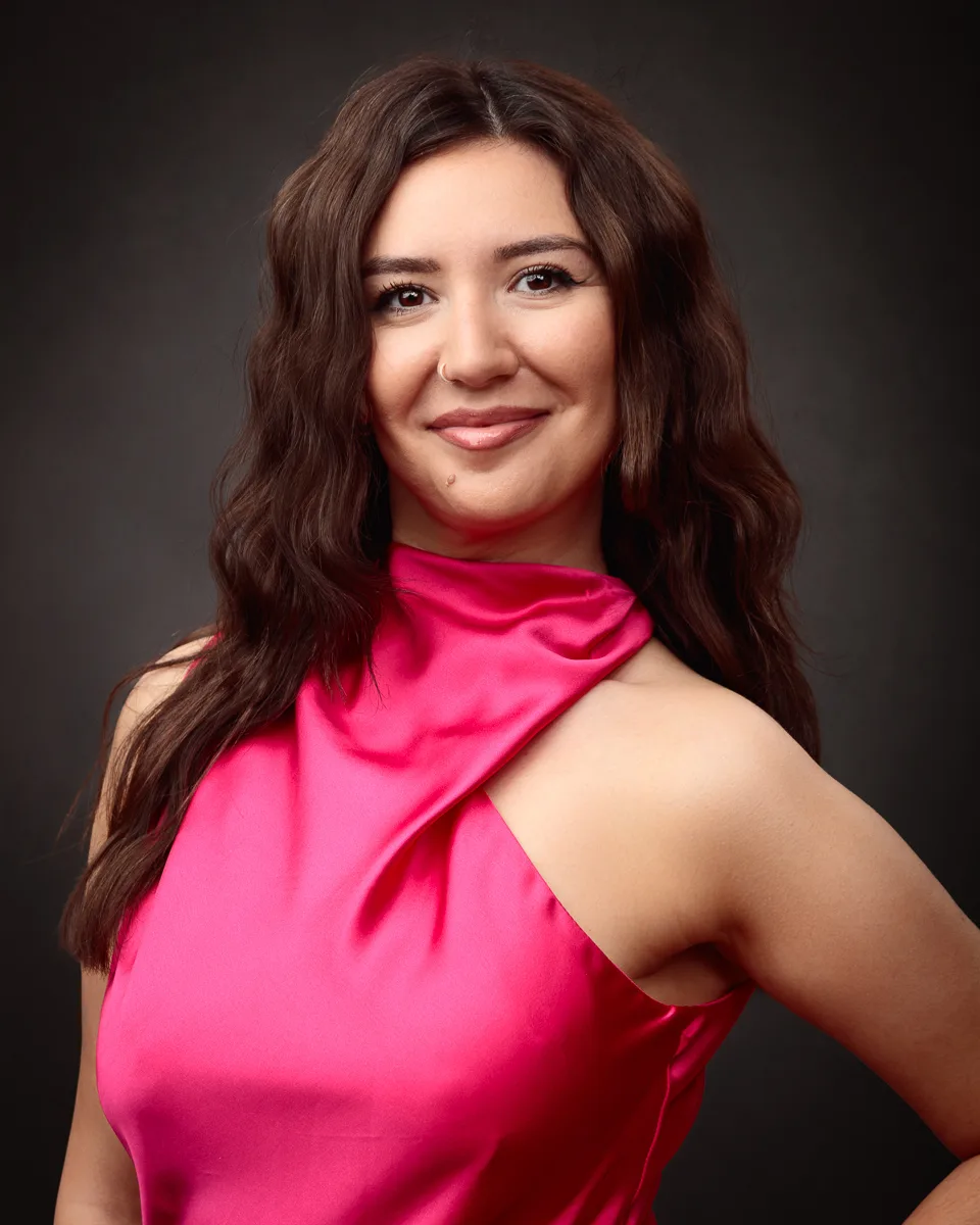 Woman in pink dress smiling against dark background.