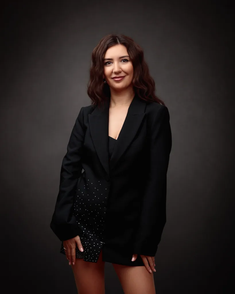 Woman in black blazer, smiling against dark background.