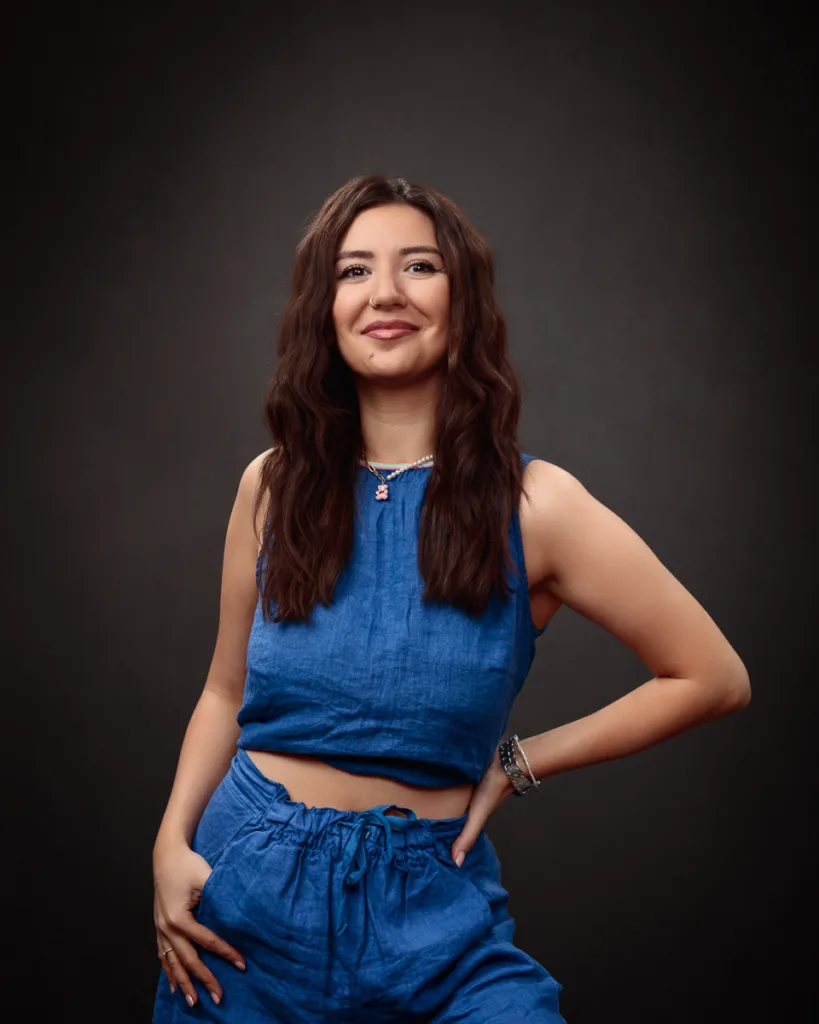 Smiling person in blue outfit, dark background.