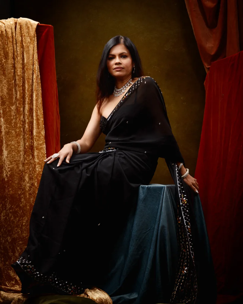 Woman in black sari with ornate jewellery seated elegantly.
