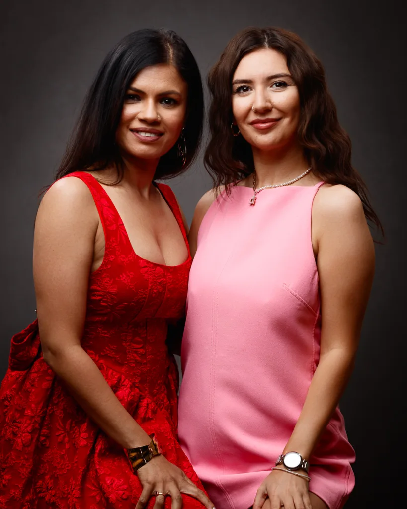 Two women in red and pink dresses smiling.