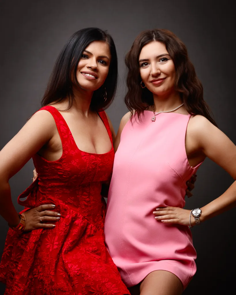 Two women in red and pink dresses posing together.