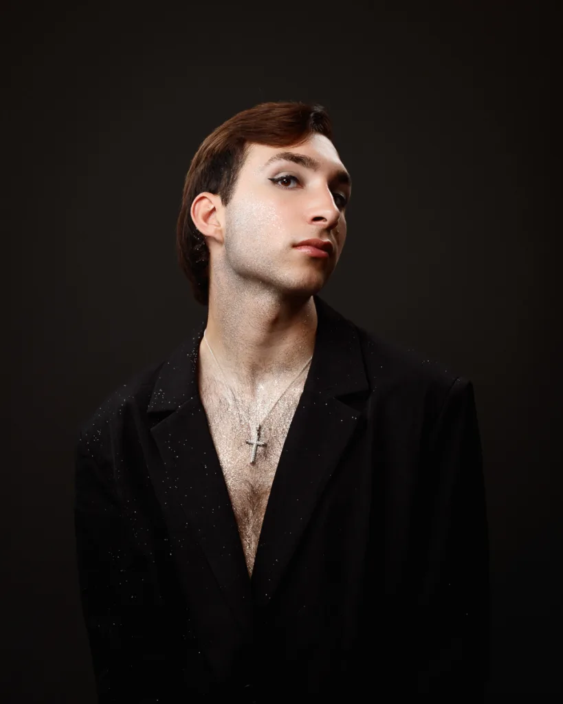 Person in black blazer with glitter and necklace.