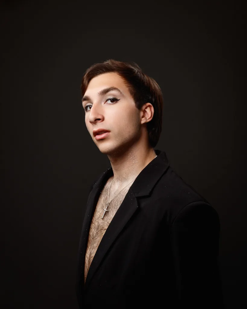 Person posing in black suit, dramatic lighting.