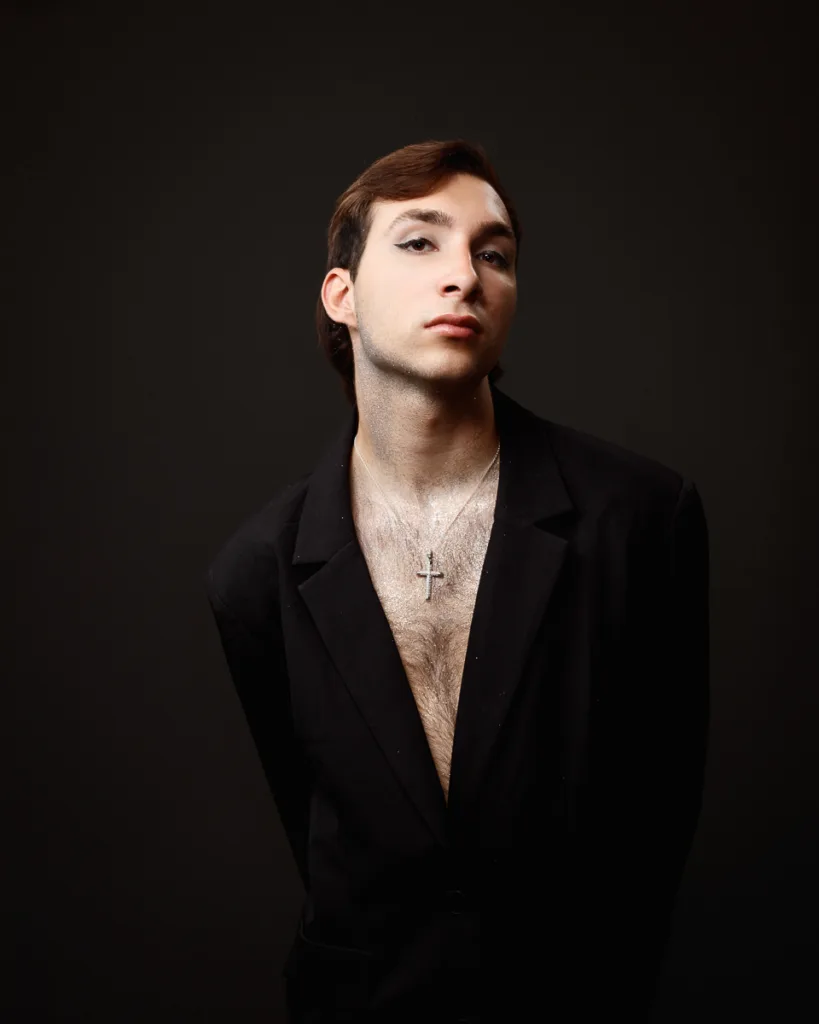 Stylish person in black suit with cross necklace.