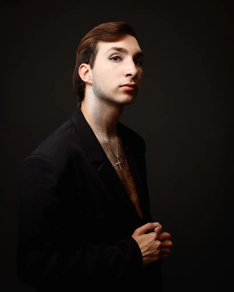 Person in black jacket with glitter and cross necklace.
