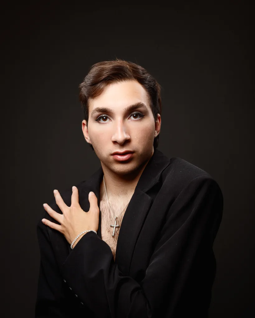 Person in black suit, wearing cross necklace.