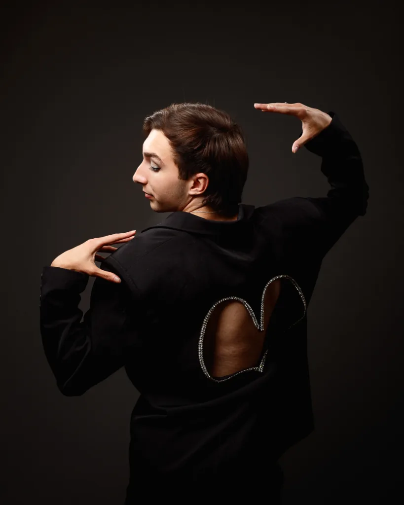 Dancer posing in elegant, embellished black suit.