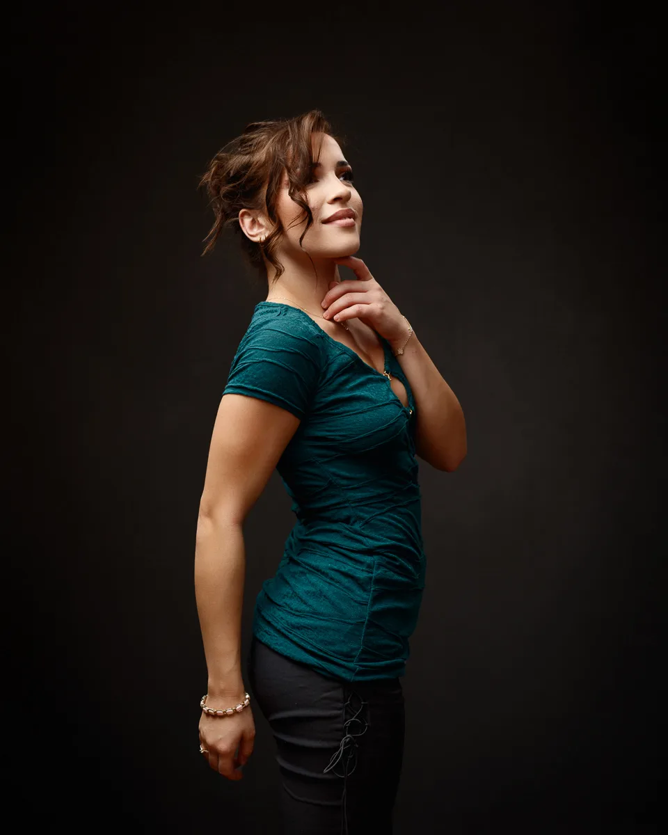 Woman posing in elegant teal top, dark background.