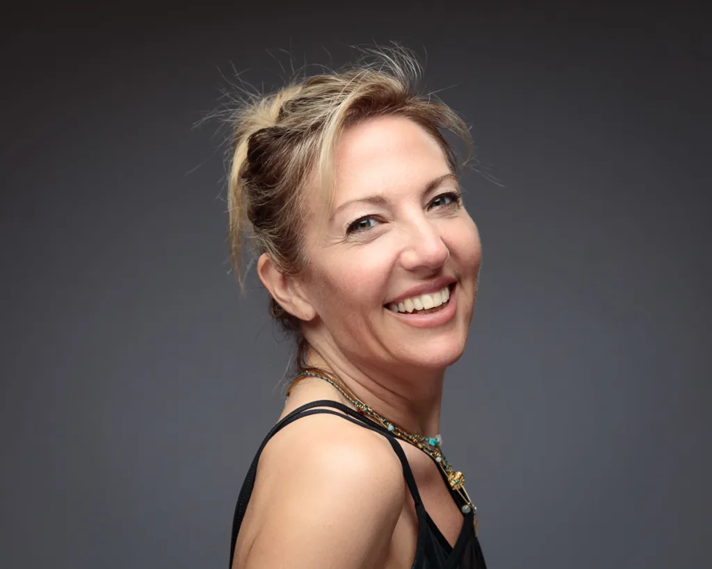 Smiling woman in black top, dark background.