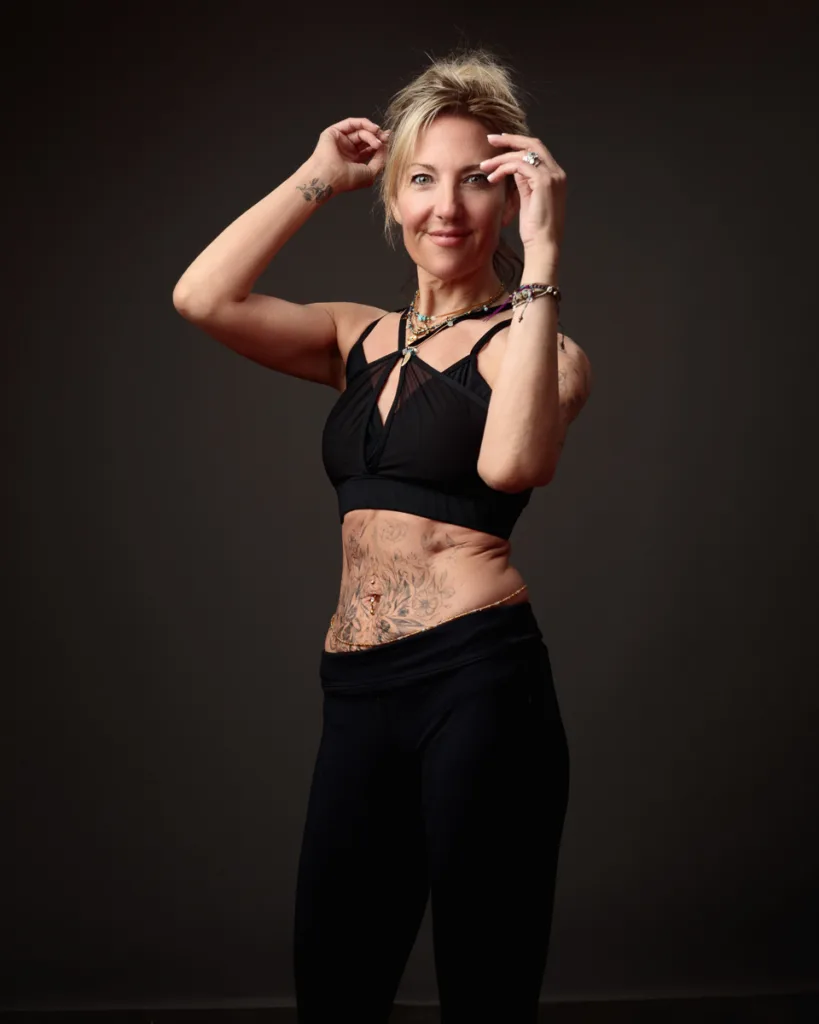 Woman in black attire with tattoos posing confidently.