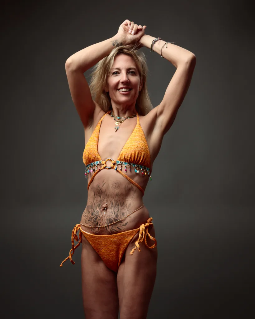 Woman in orange bikini with tattoos posing confidently.