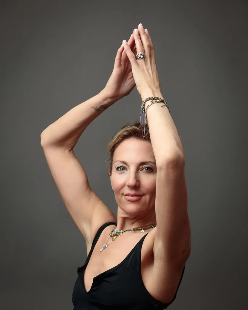 Woman posing with arms raised, wearing jewellery.
