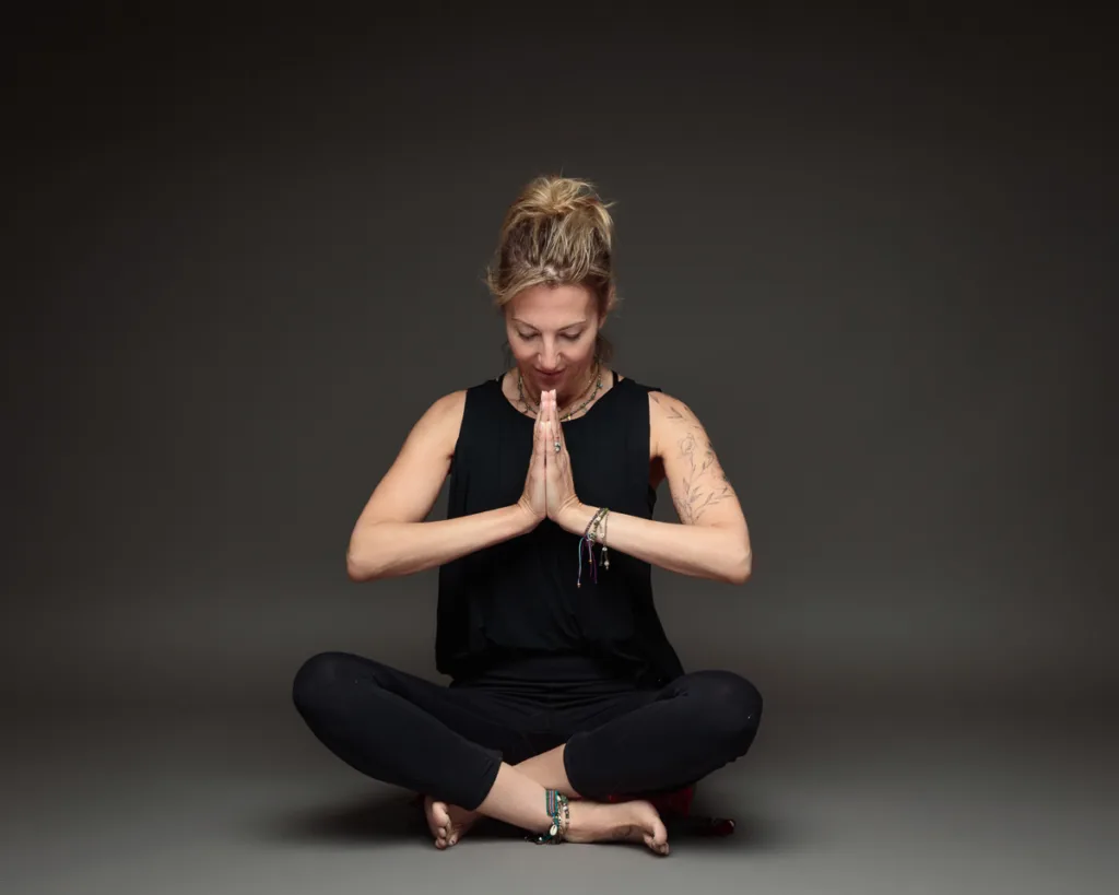 Person meditating in lotus position, hands in prayer.