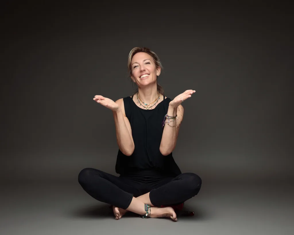 Smiling woman seated cross-legged on grey background.
