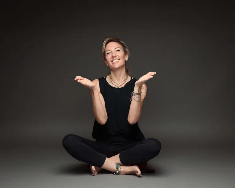 Smiling woman seated cross-legged on grey background.