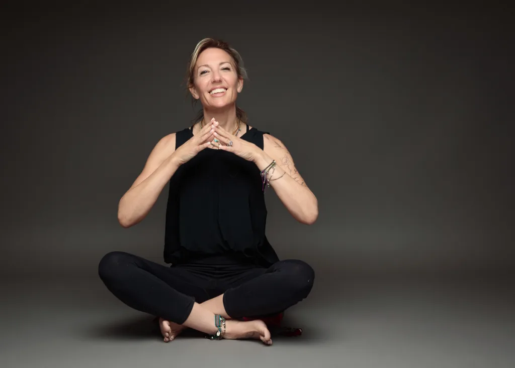 Smiling woman sitting cross-legged, hands clasped.
