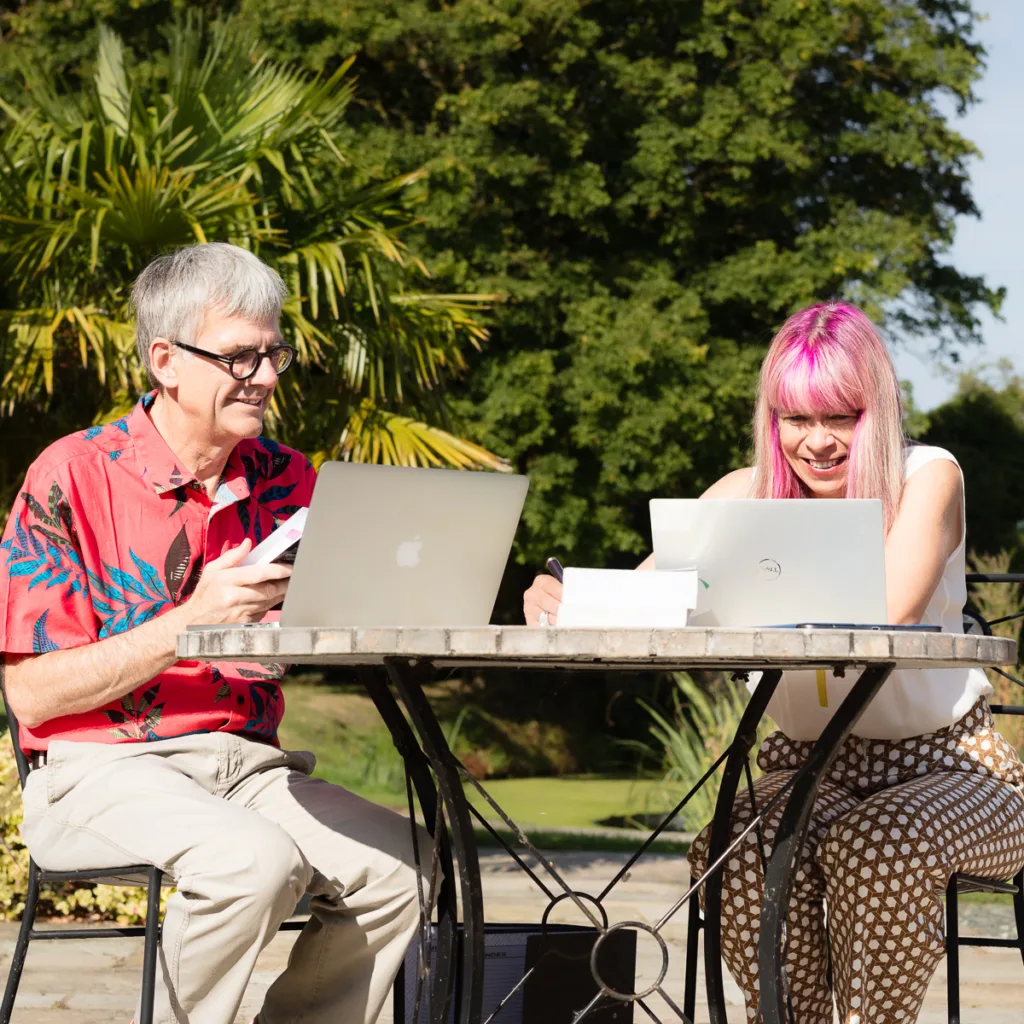 Two people working outdoors with laptops.