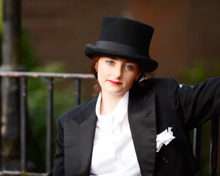 Person in suit and top hat outdoors.