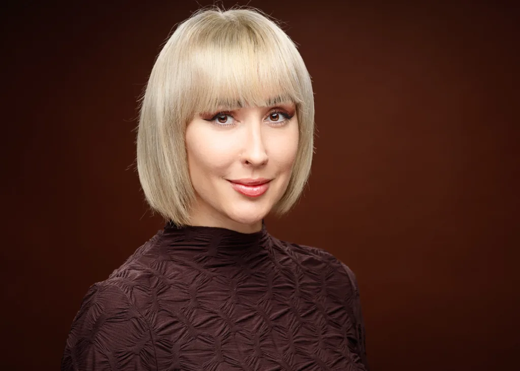 Woman with short blonde hair, wearing a brown top.