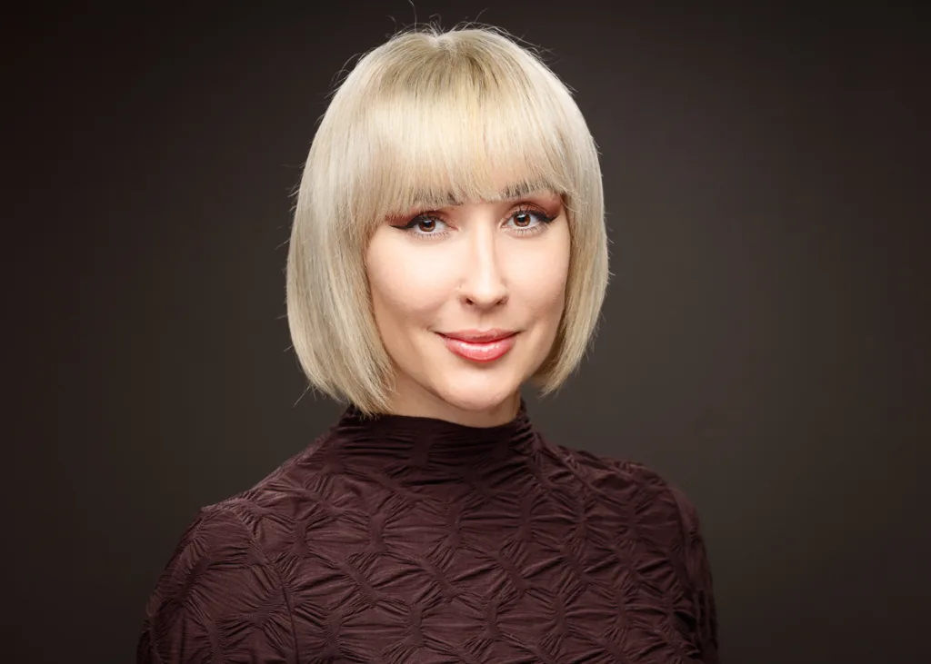 Woman with short blonde hair, wearing a dark top.