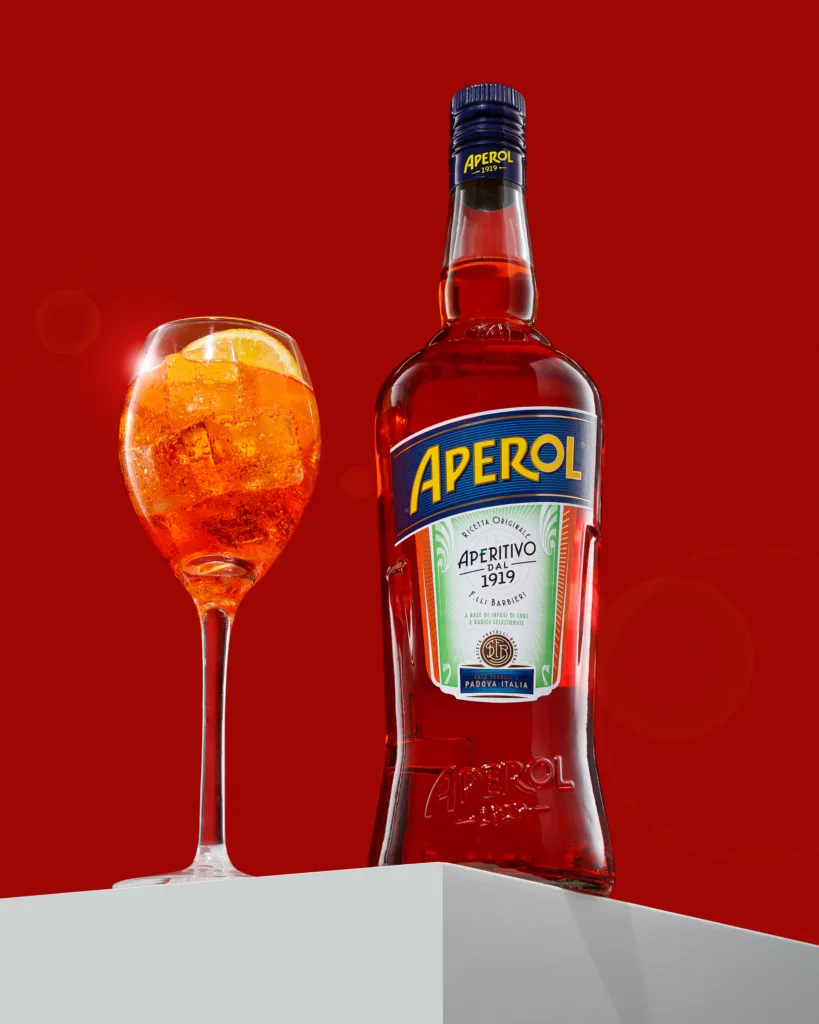 Aperol bottle and spritz glass on red backdrop.
