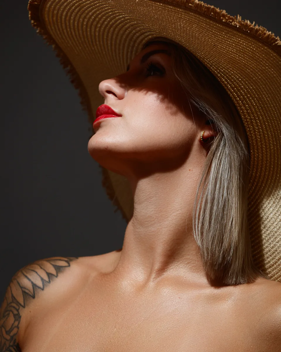 Woman in straw hat looking upwards, tattoo on shoulder.
