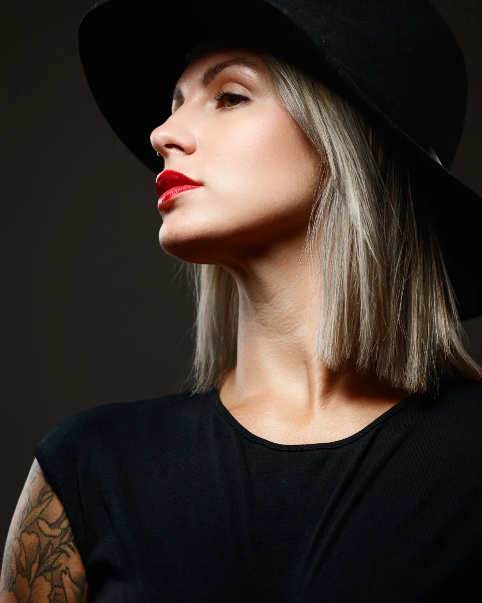 Woman in black hat with tattoo, grey background.